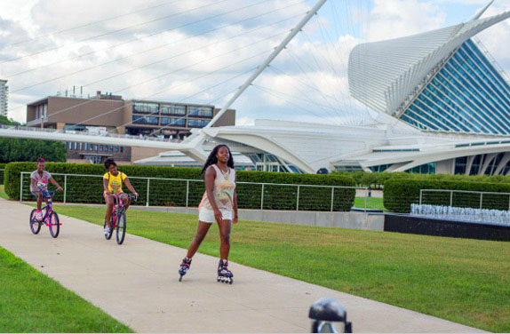 Three friends rollerblading and biking past the Milwaukee Art Museum